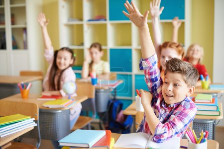 Boy raising hand at workplace with classmates