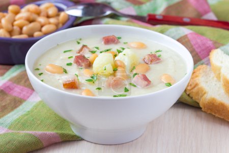 Cream soup with cauliflower, white beans and fried bacon in whit