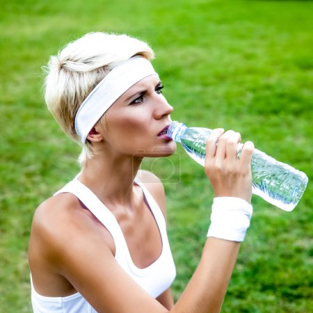 Young woman drinking water at workout outdoors