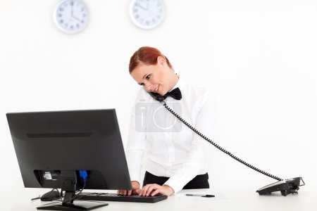 Hotel receptionist talking on phone while checking on computer