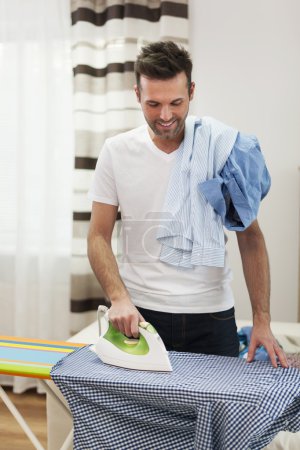 Smiling man ironing his shirts