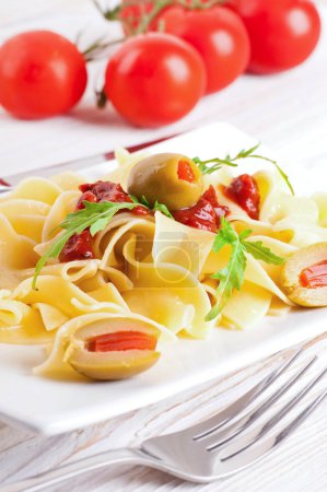 Pasta with tomato and arugula on the wooden table