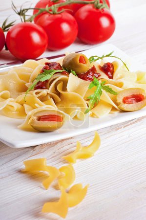 Pasta with tomato and arugula on the wooden table