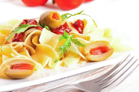 Pasta with tomato and arugula on the wooden table