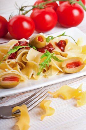 Pasta with tomato and arugula on the wooden table