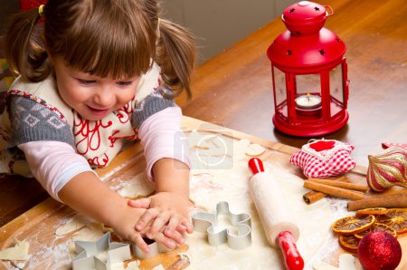 Little girl baking Christmas cookies cutting pastry with a cooki