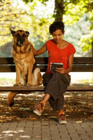 Woman on a bench with digital tablet and dog