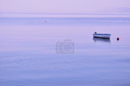 Small lonely fishing boat floating on flat surface of sea