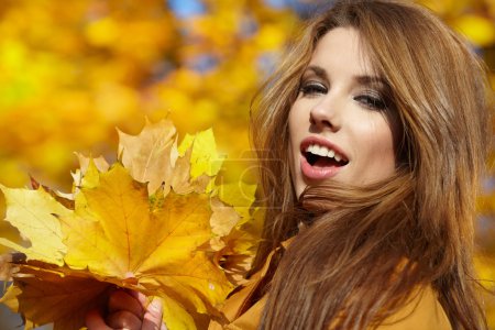 Young woman with autumn leaves in hand and fall yellow maple gar