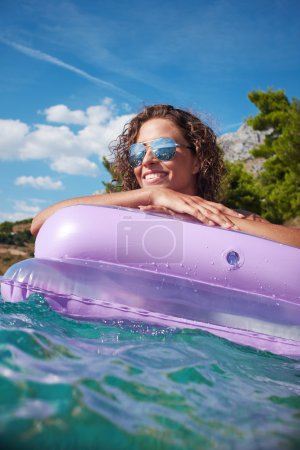 Woman having fun on pink air bed in sea