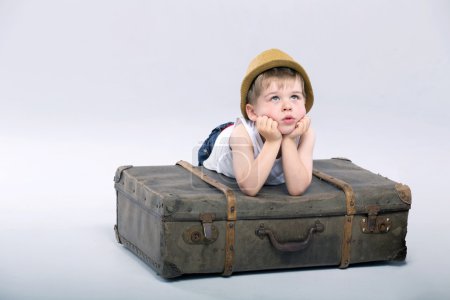 Thoughtful boy lying on the suitcase