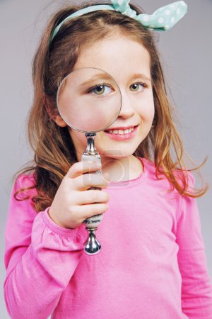 Beautiful little girl looking through a magnifying glass