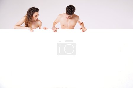 Man and woman looking behind white panel isolated on white backg
