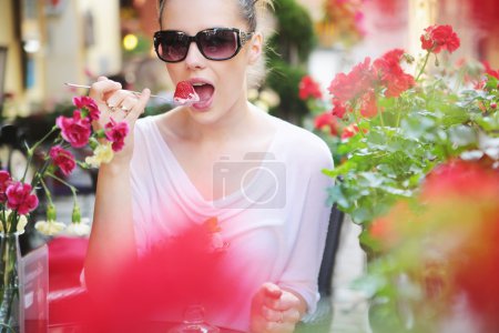 Delighted brunette lady eating sweet strawberry