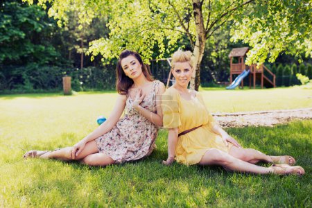 Two romantic ladies sitting on flower meadow