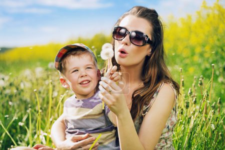 Pretty young mother playing dandelions with son