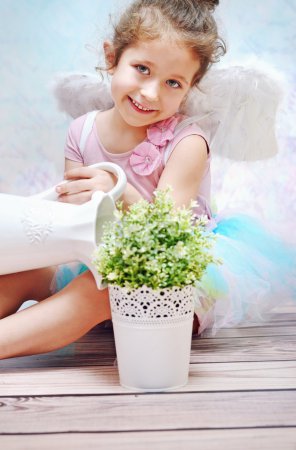 Little smiling girl watering plant