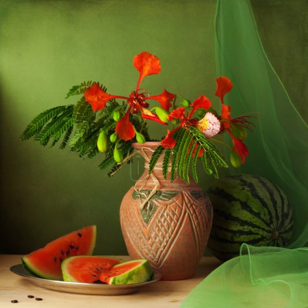 Still life with water melon and red flowers over green background