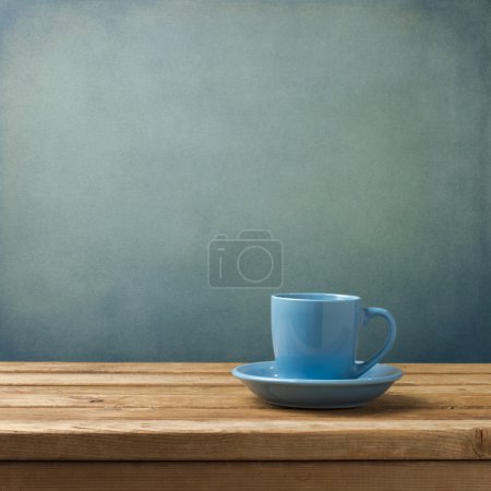 Blue coffee cup on wooden table over blue grunge background