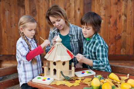 Woman with kids painting the bird house - preparing for winter