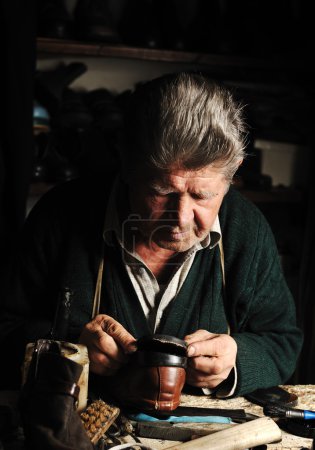 Old man, shoemaker, repairing old handmade shoe in his workshop