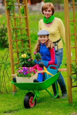 Gardening - lovely girl with mother working in flowers garden