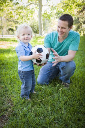 Young Boy and Dad Playing with Soccer Ball in Park