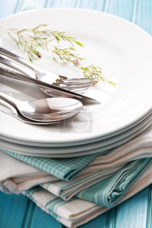 A stack of clean white plates with sliverware