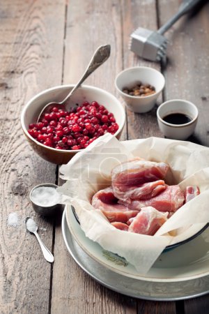 Raw pork in a bowl, cranberries, seasonings and meat hammer on w