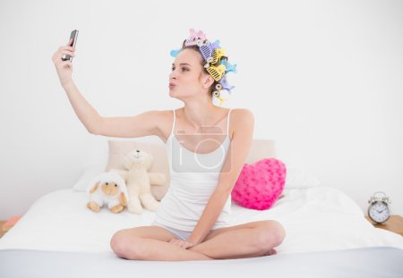 Woman in hair curlers taking a picture of herself with mobile phone