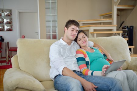 pregnant couple at home using tablet computer