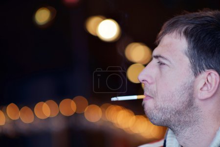 man smokes a cigaret against a dark background