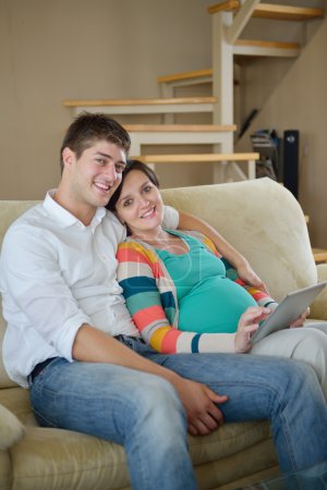 Pregnant couple at home using tablet computer