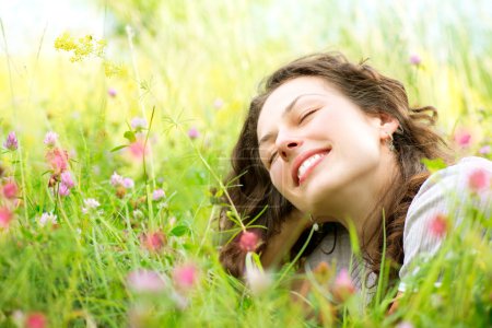 Beautiful Young Woman lying in Meadow of Flowers. Enjoy Nature