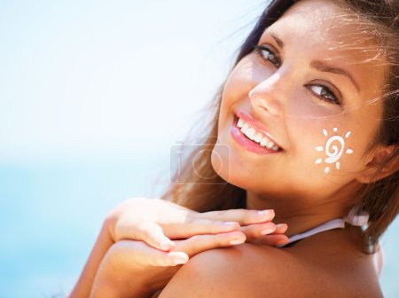 Beautiful happy Girl applying Sun Tan Cream on her Face