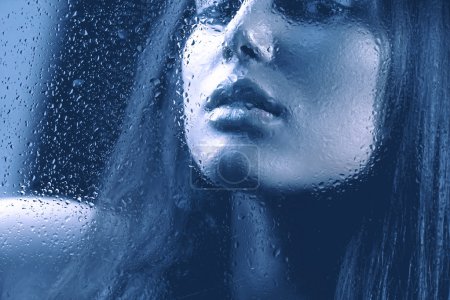 Portrait of Beauty Girl behind the Wet Glass