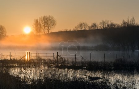 Landscape of lake in mist with sun glow at sunrise