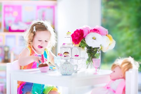 Toddler girl playing tea party with a doll