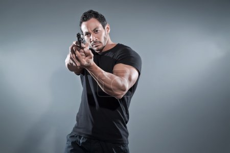 Action hero muscled man shooting with gun. Wearing black t-shirt