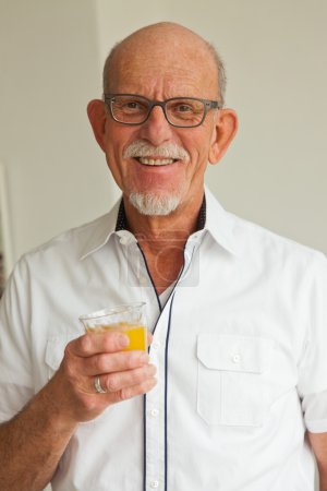 Senior man with glasses drinking orange juice in living room.