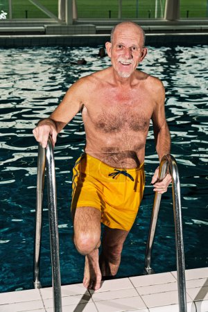 Senior man walking out of swimming pool. Wearing yellow swimming