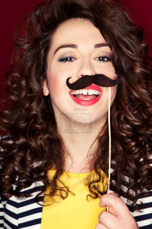 Attractive playful young woman holding mustache on a stick