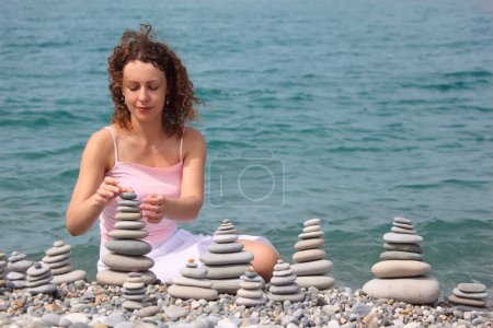 Young woman builds stone stacks on pebble beach