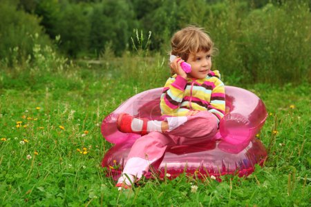 Little girl sits talks by toy phone in inflatable armchair on l
