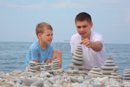 Father and son builds stone stacks on pebble beach