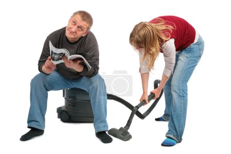 Woman vacuums, man sits on vacuum cleaner with magazine