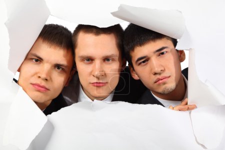 Three young men looking out in hole in paper