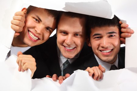 Three young smiling men looking out in hole in paper