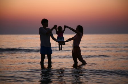 Father with mother hold child in sea on sunset