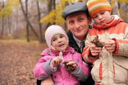 Grandfather with grandsons in forest in autumn with burr in hand
